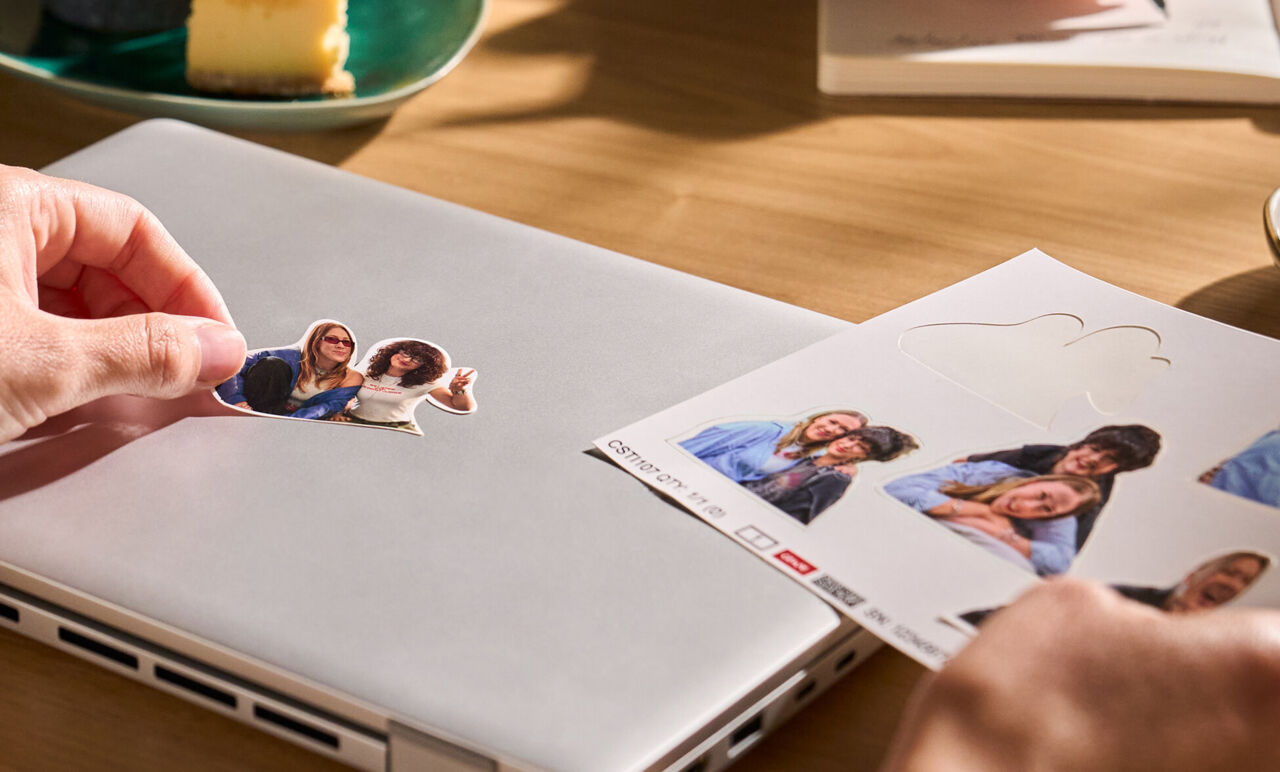 Eine Hand platziert einen personalisierten Freiform Sticker auf einem Laptop.