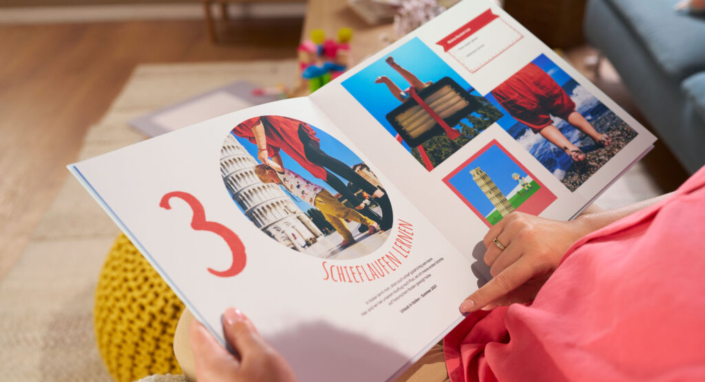 Eine Frau sitzt auf einem Sofa und blättert durch ein CEWE FOTOBUCH, die Doppelseite zeigt Fotomotive und die Zahl „3“.