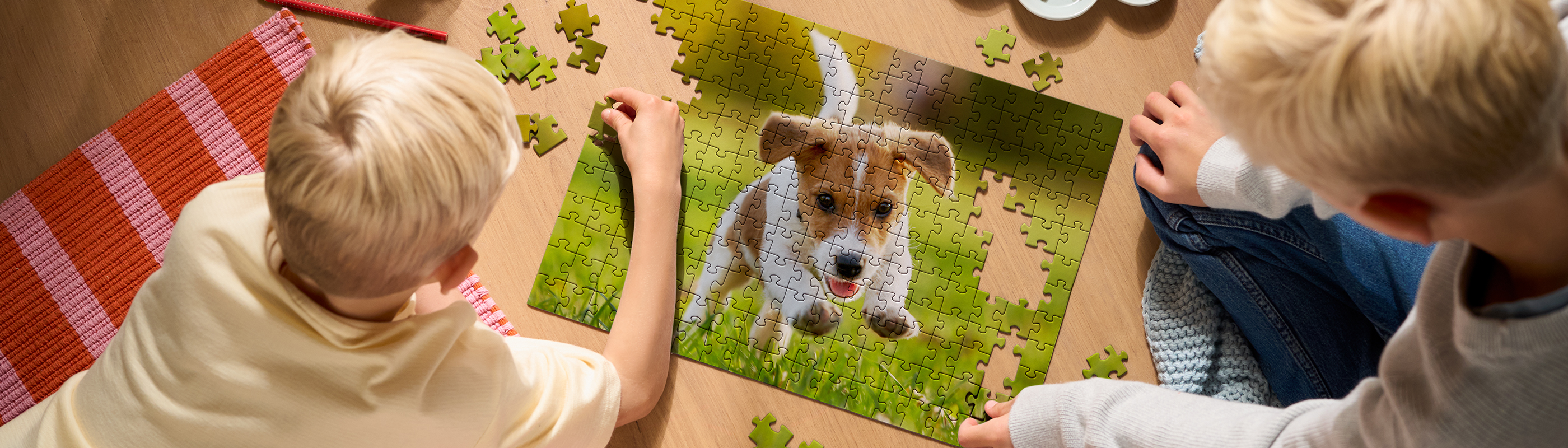 Zwei Kinder setzen gemeinsam ein Premium Fotopuzzle mit Hundemotiv auf dem Boden zusammen.