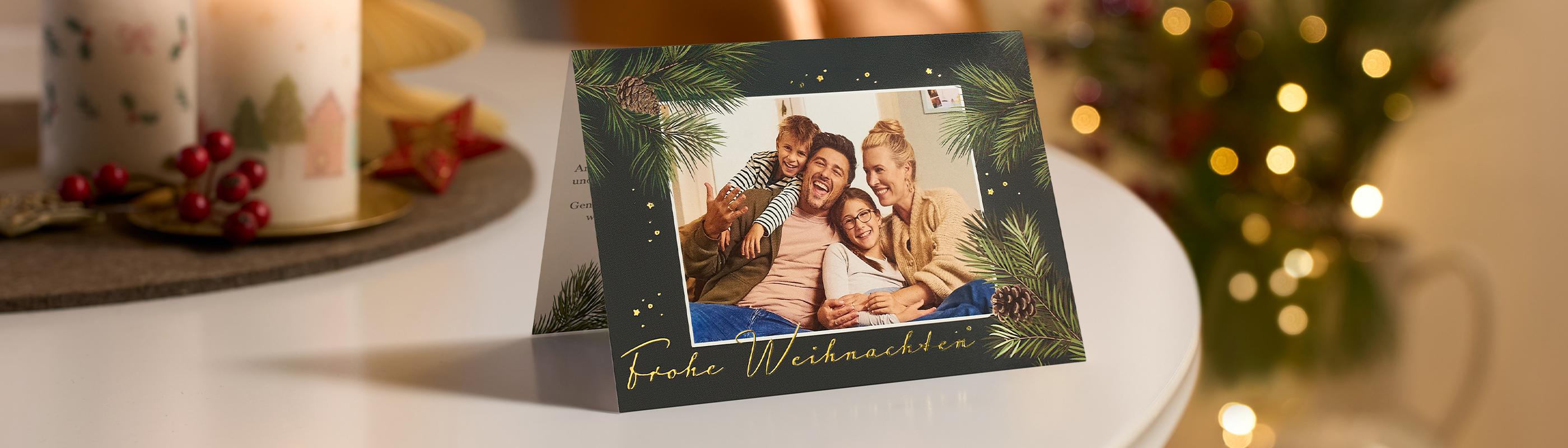 CEWE Grußkarte mit Familienfoto und Weihnachtsgrüßen neben einem geschmückten Weihnachtsbaum.