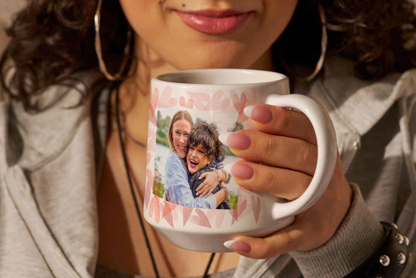 Eine Person hält einen personalisierten Foto-Kaffeebecher mit einem Foto von zwei lächelnden Personen.