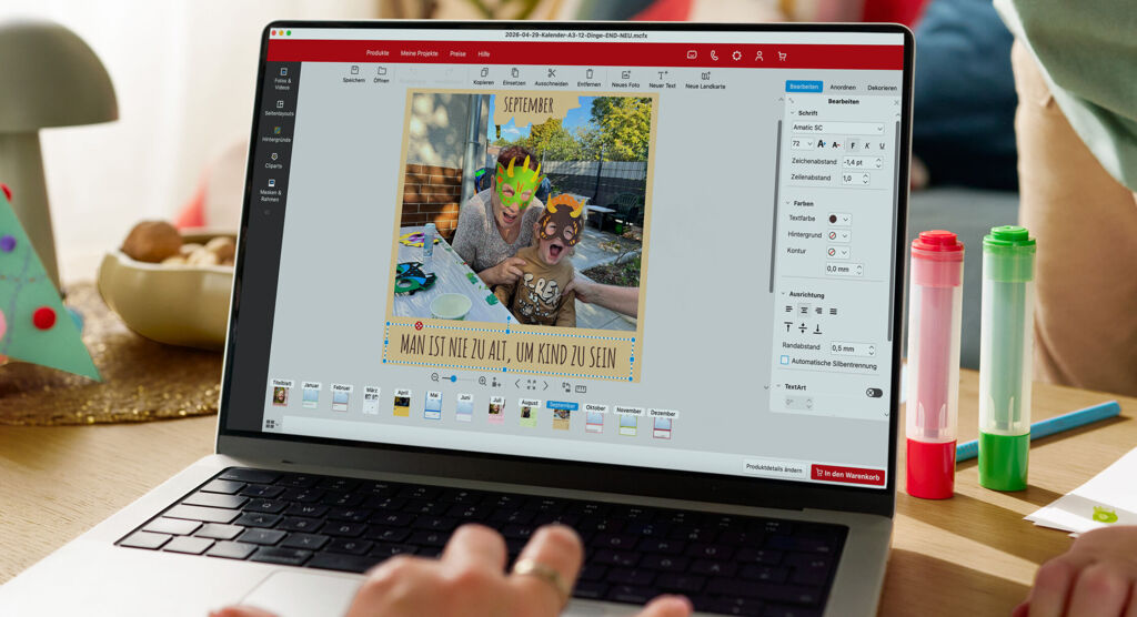 Eine Frau sitzt vor einem Laptop und gestaltet einen Fotokalender. Im Hintergrund ist ein spielendes Kind zu sehen.