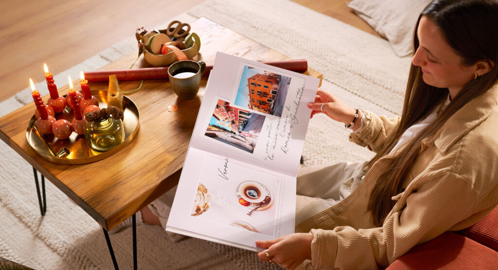 Eine Frau hält ein CEWE FOTOBUCH in den Händen, in dem mehrere Fotomotive und Schrift-Elemente zu sehen sind.