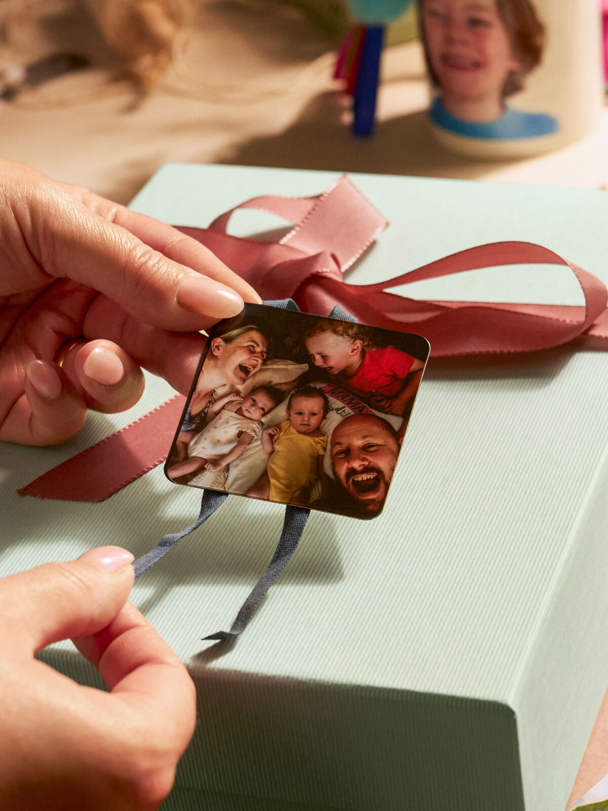 Eine Person befestigt zwei Magneten mit Fotomotiven als Anhänger an einem Geschenk.