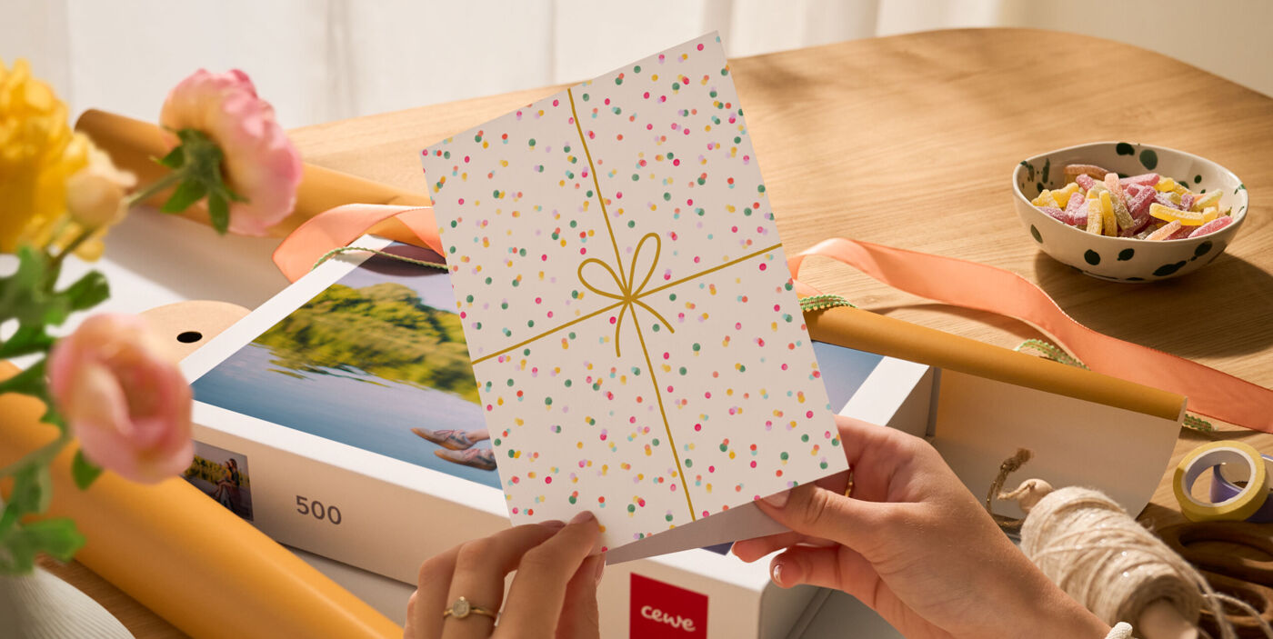 Hände halten eine gepunktete Grußkarte vor einem CEWE Fotopuzzle mit 500 Teilen