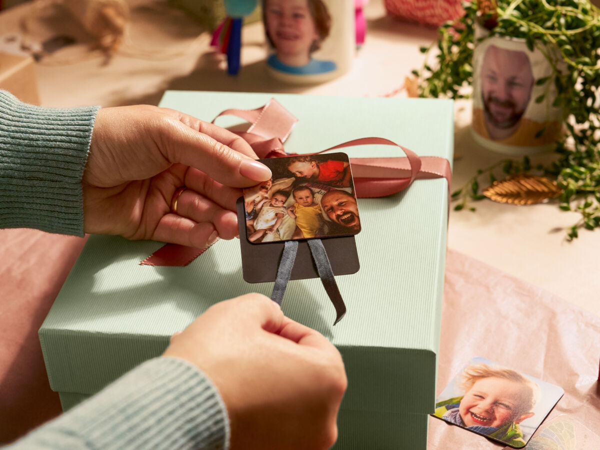 Eine Person befestigt zwei Magneten mit Fotomotiven als Anhänger an einem Geschenk.